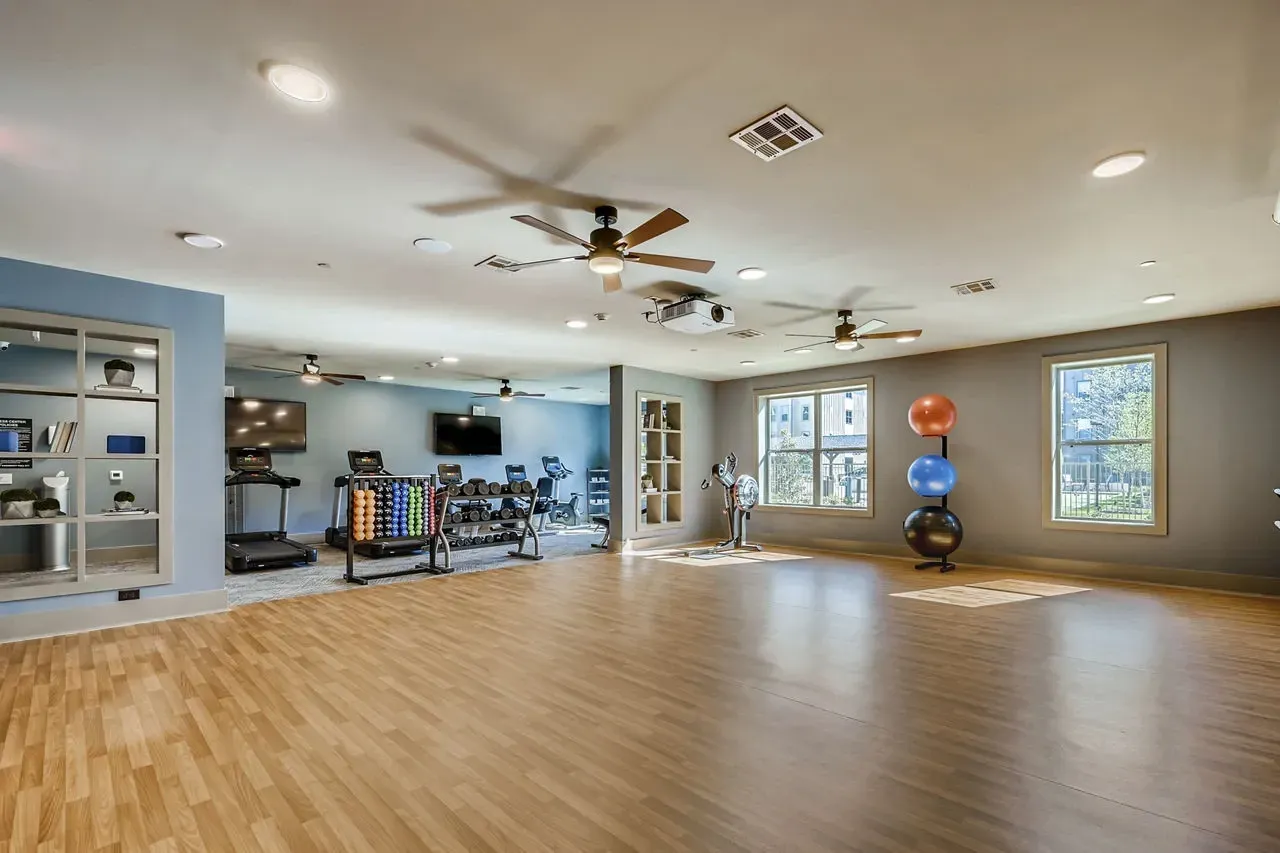 Indoor gym area with hardwood floor, ceiling fans, and fitness equipment like treadmills and free weights.