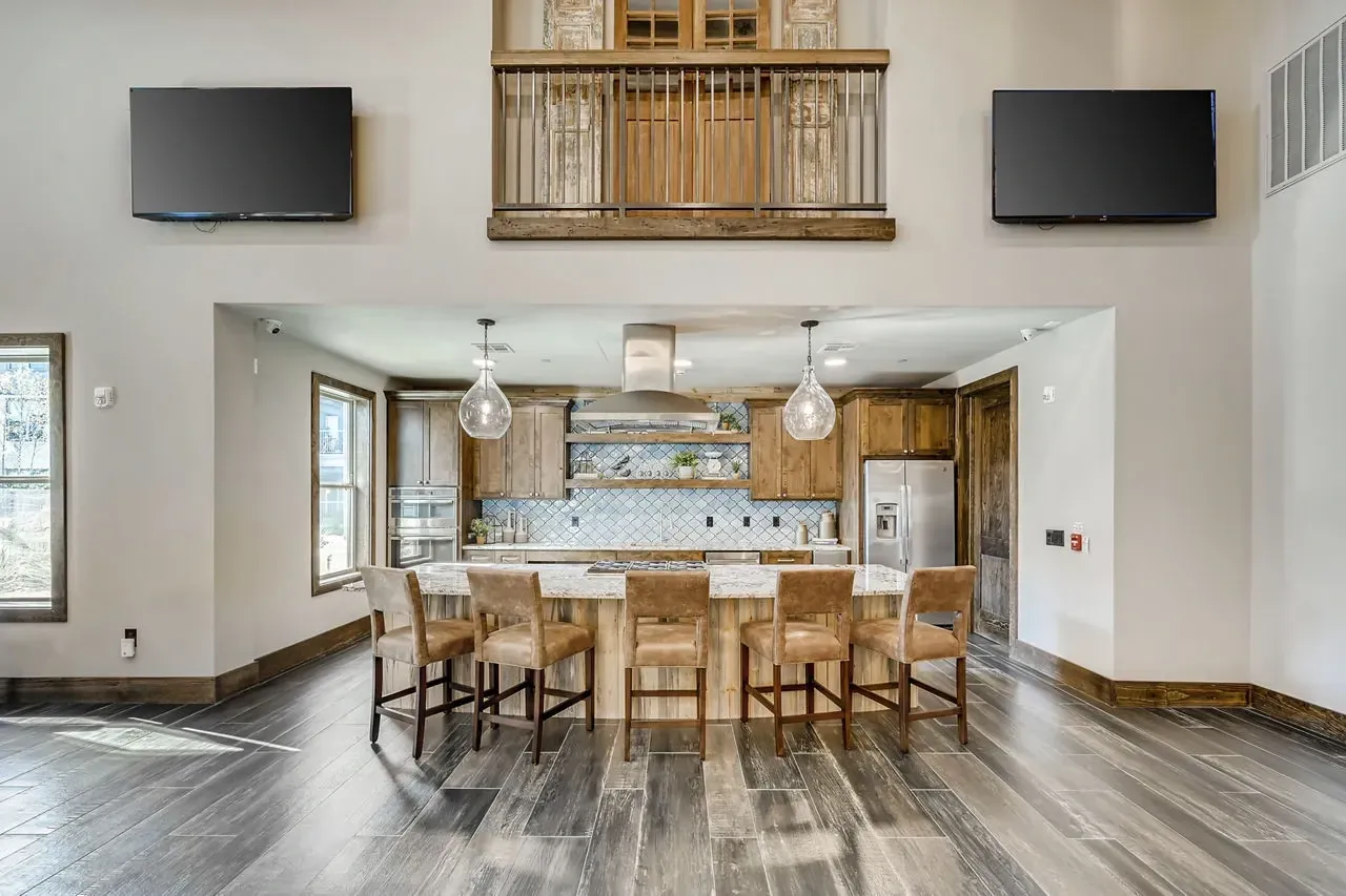 Open-concept kitchen with large island, six brown stools, stainless appliances, and a second-floor balcony.