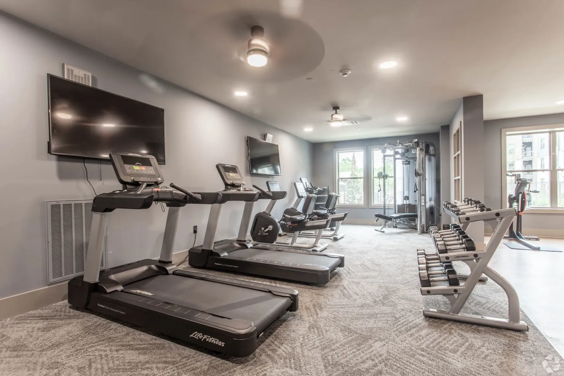 Indoor apartment gym with treadmills, weight racks, and functional training equipment.