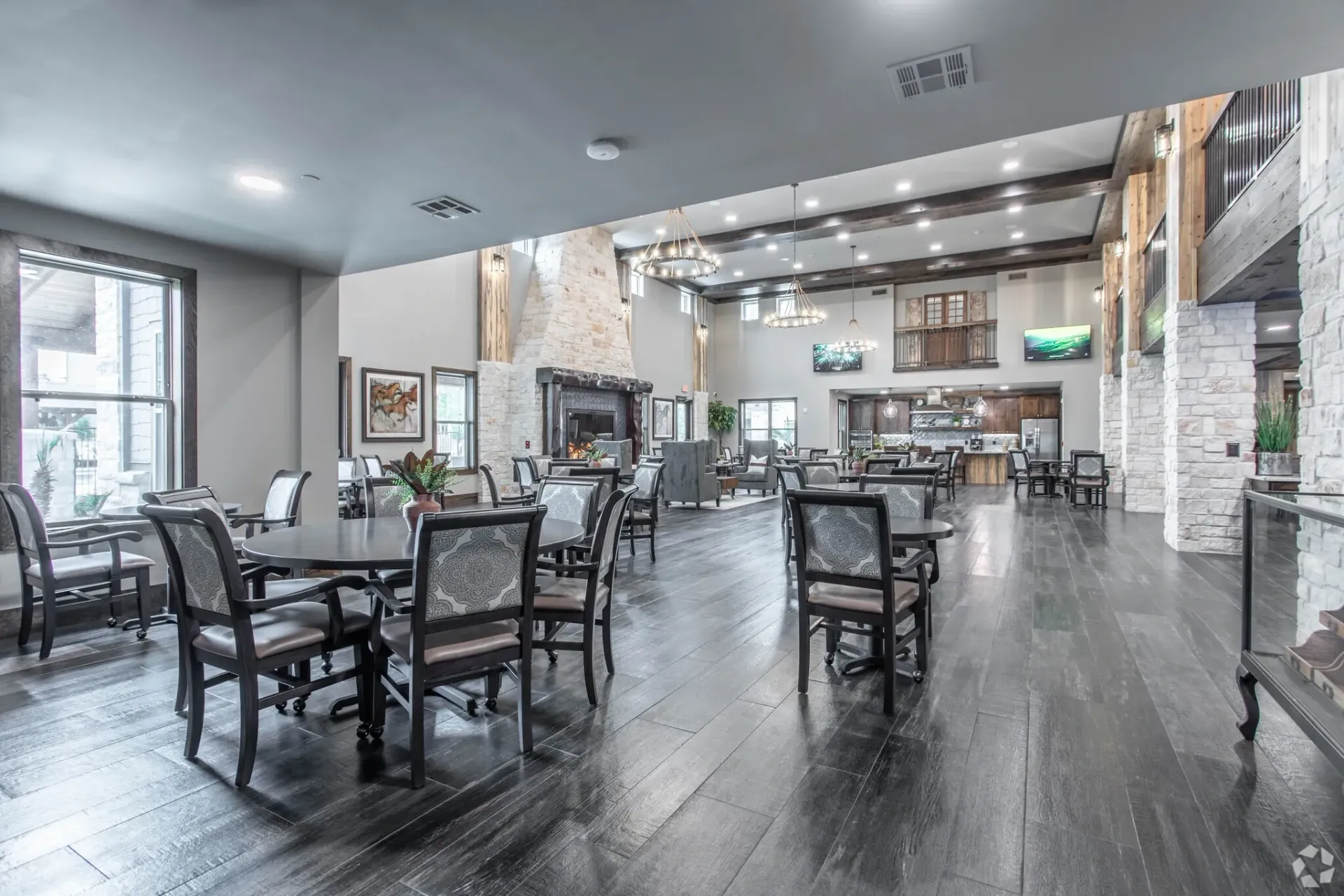 Spacious resident lounge in a clubhouse with tables, chairs, and a stone fireplace.
