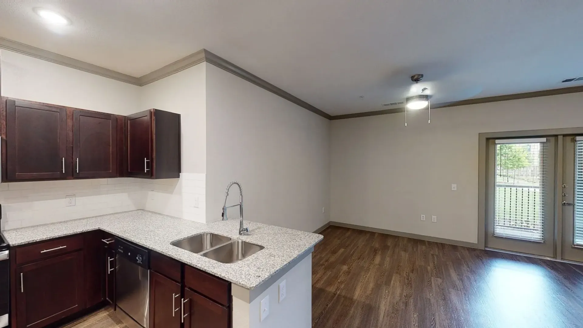 Open-concept kitchen with dark wood cabinets, granite countertops, and a stainless-steel sink, connected to the living area.
