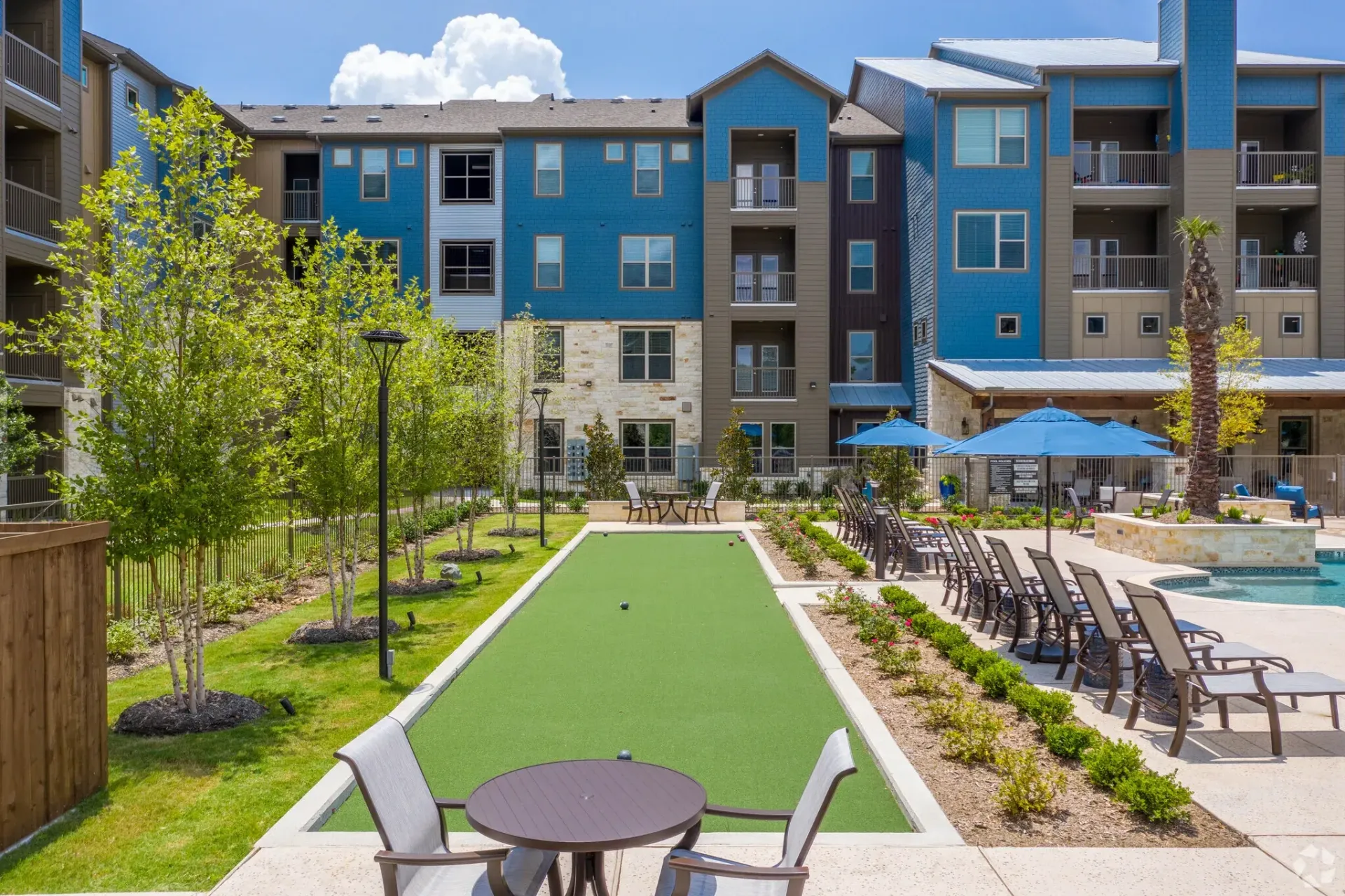 Courtyard of a multifamily community featuring a pool, lounge chairs, umbrellas, and a putting-green area.