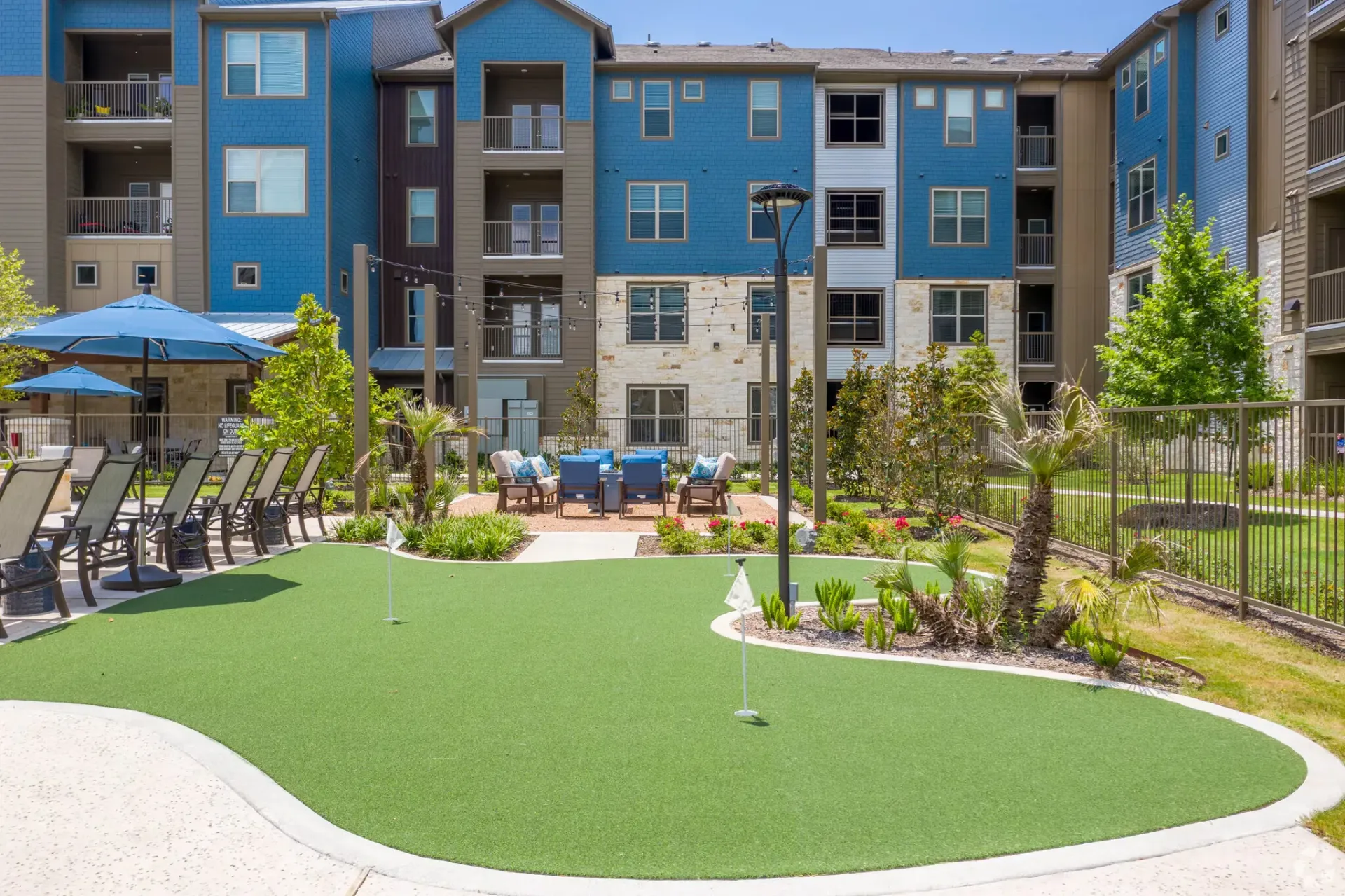 Outdoor community courtyard at a modern apartment complex with lounge seating, umbrellas, and a putting green.