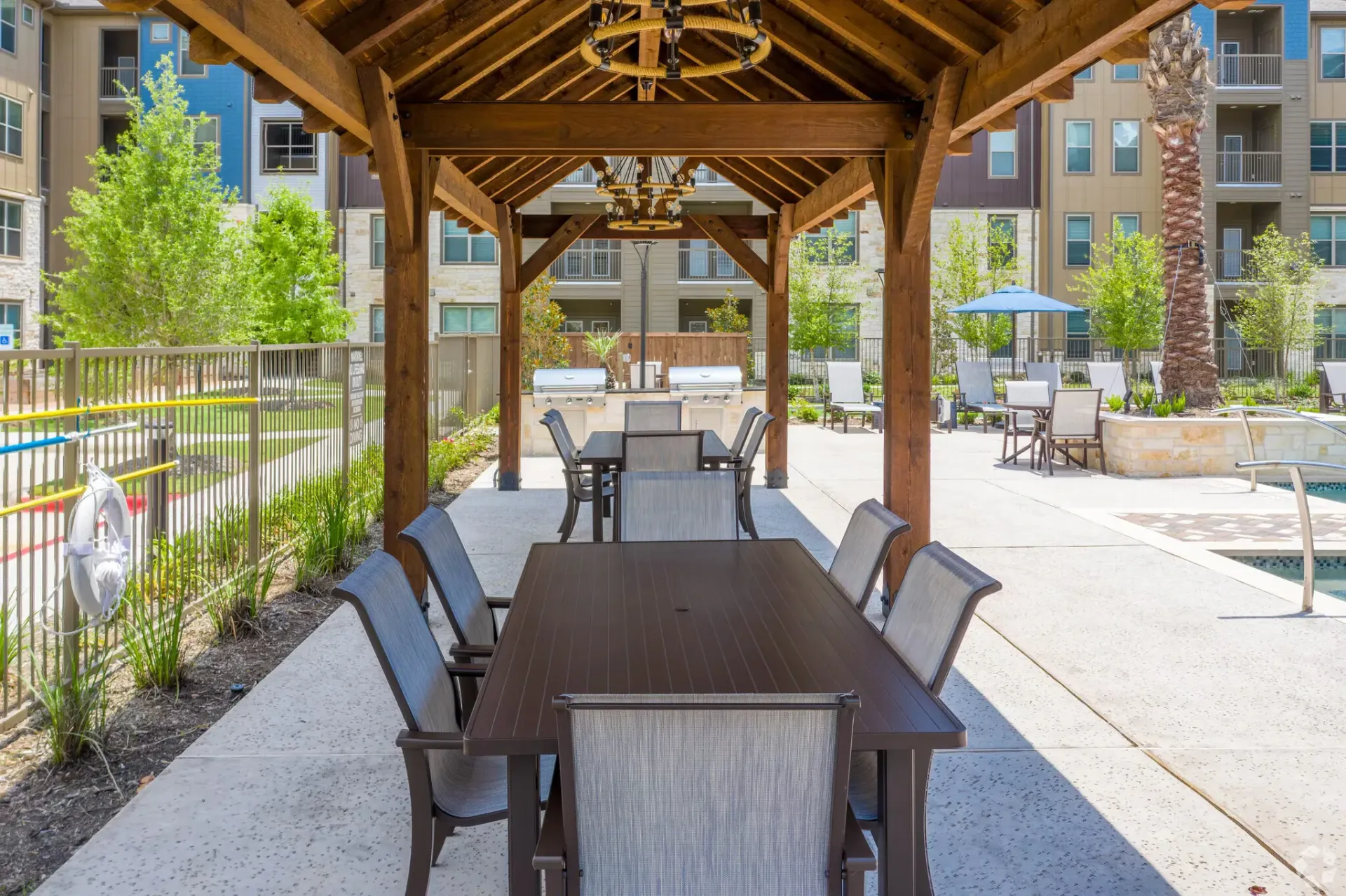 Outdoor resident gathering area under a wooden pergola with dining tables and chairs.