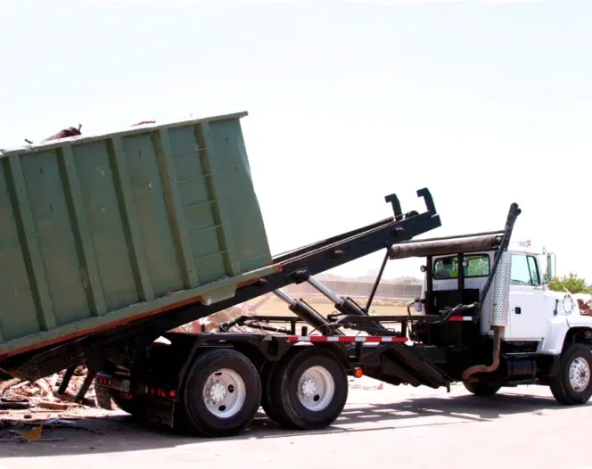 A dump truck is pulling a large green dumpster