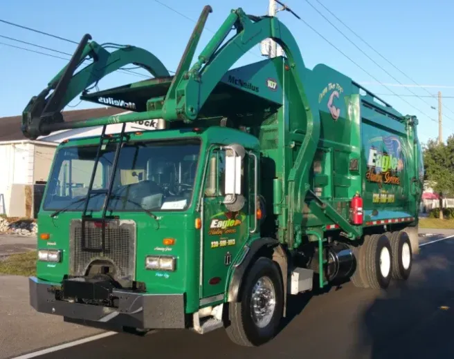 A green garbage truck is parked on the side of the road