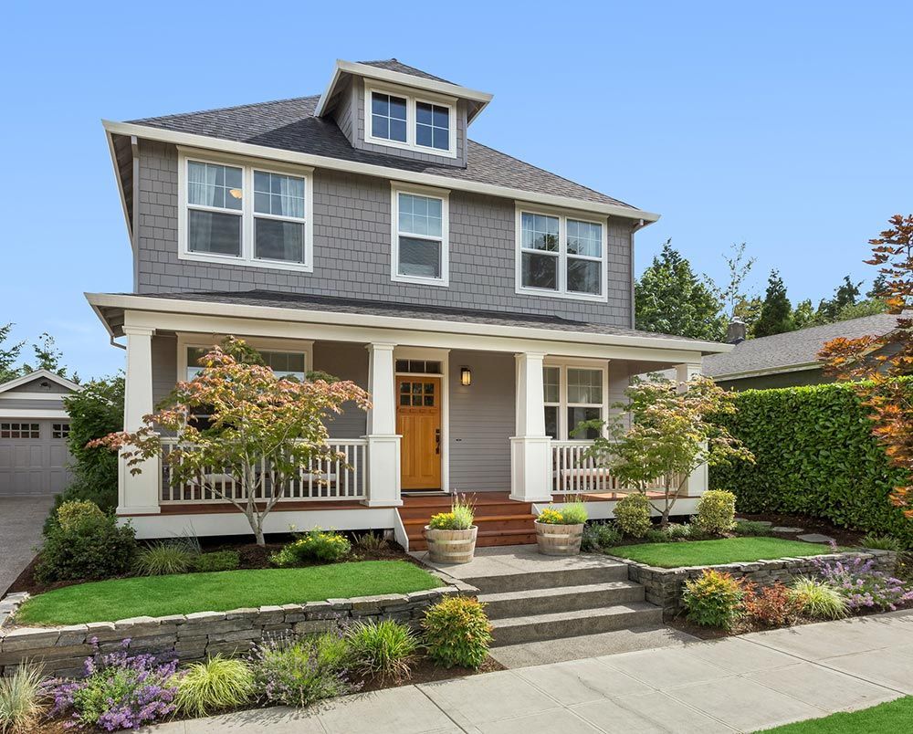 A large gray house with a large porch and stairs leading up to it.