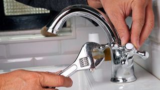 A person is fixing a sink faucet with a wrench.