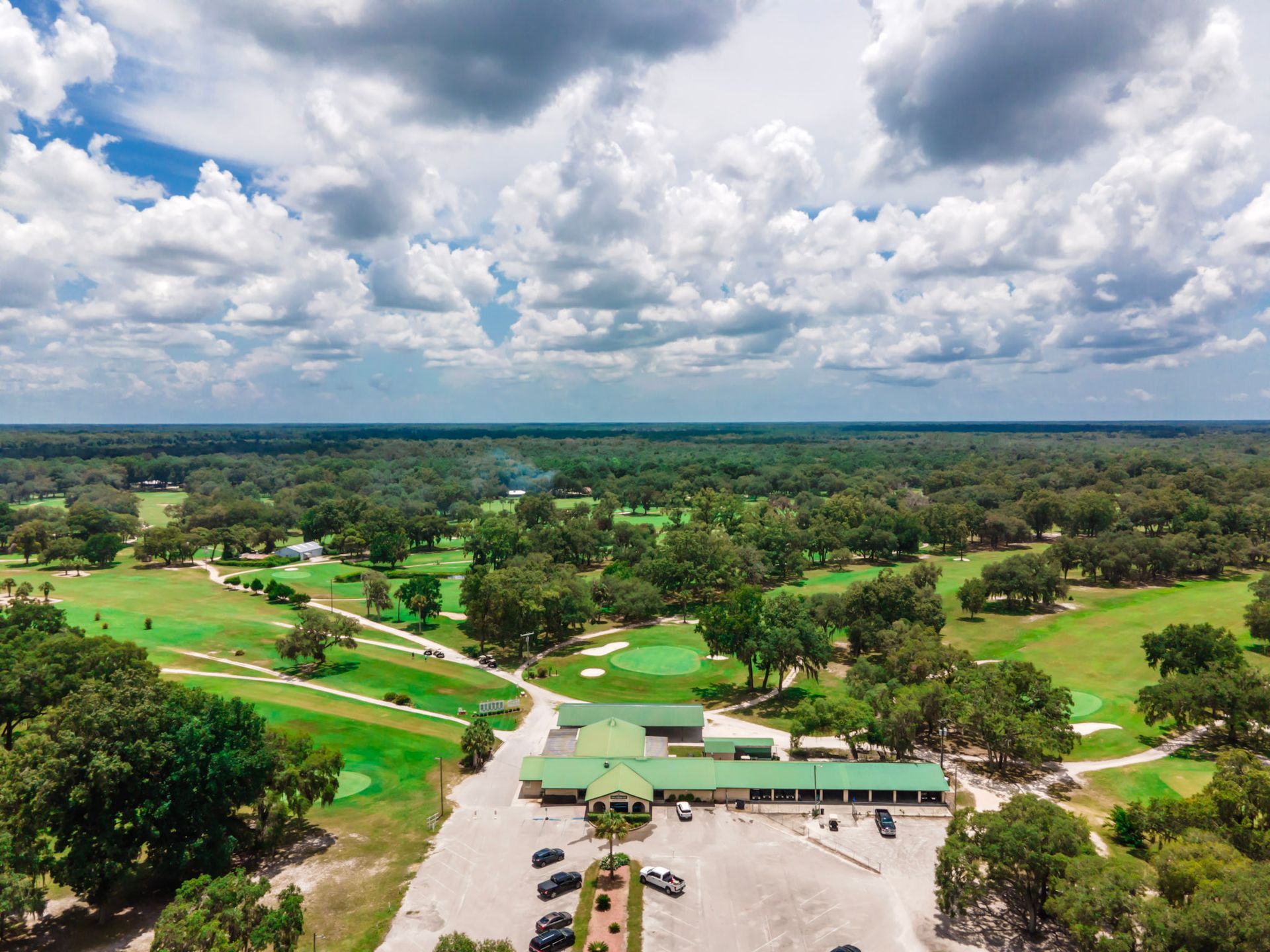 An aerial view of a golf course surrounded by trees on a cloudy day.