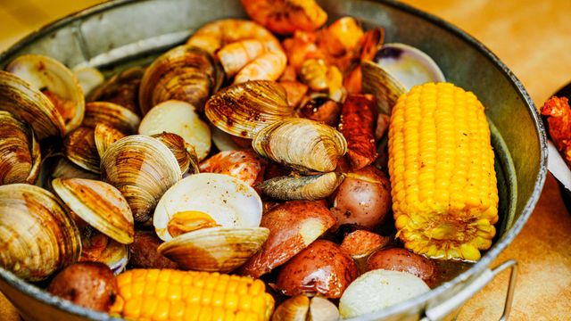 A bucket filled with clams , shrimp , corn on the cob and potatoes.