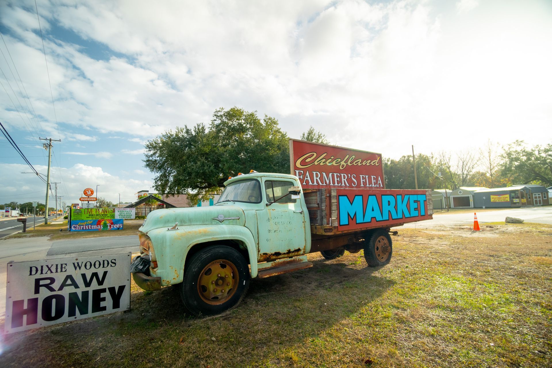 An old truck is parked in front of a sign that says raw honey market.