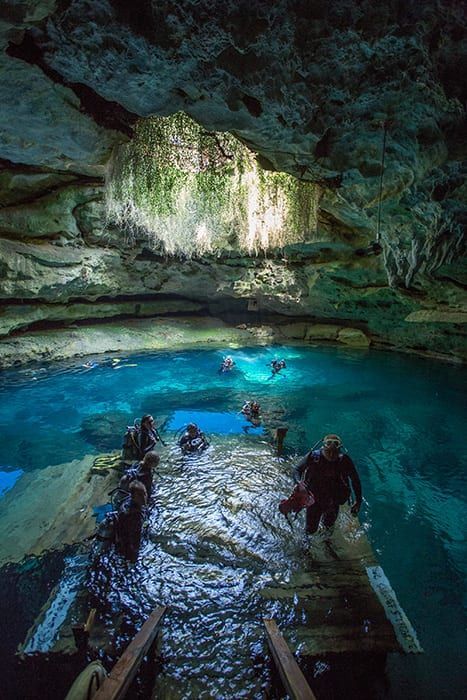 A group of people are walking down stairs into a cave filled with water.