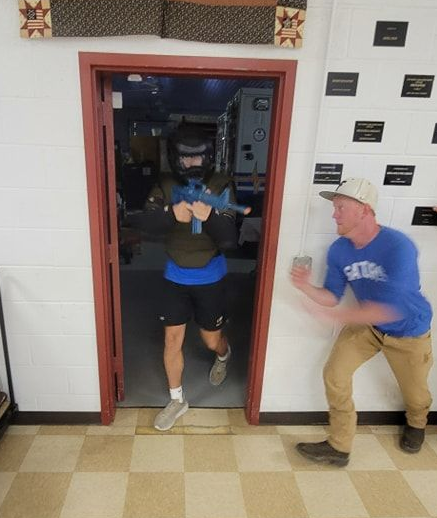 Two men in a gym practice martial arts. The man on the left punches toward the other man's outstretched hand.