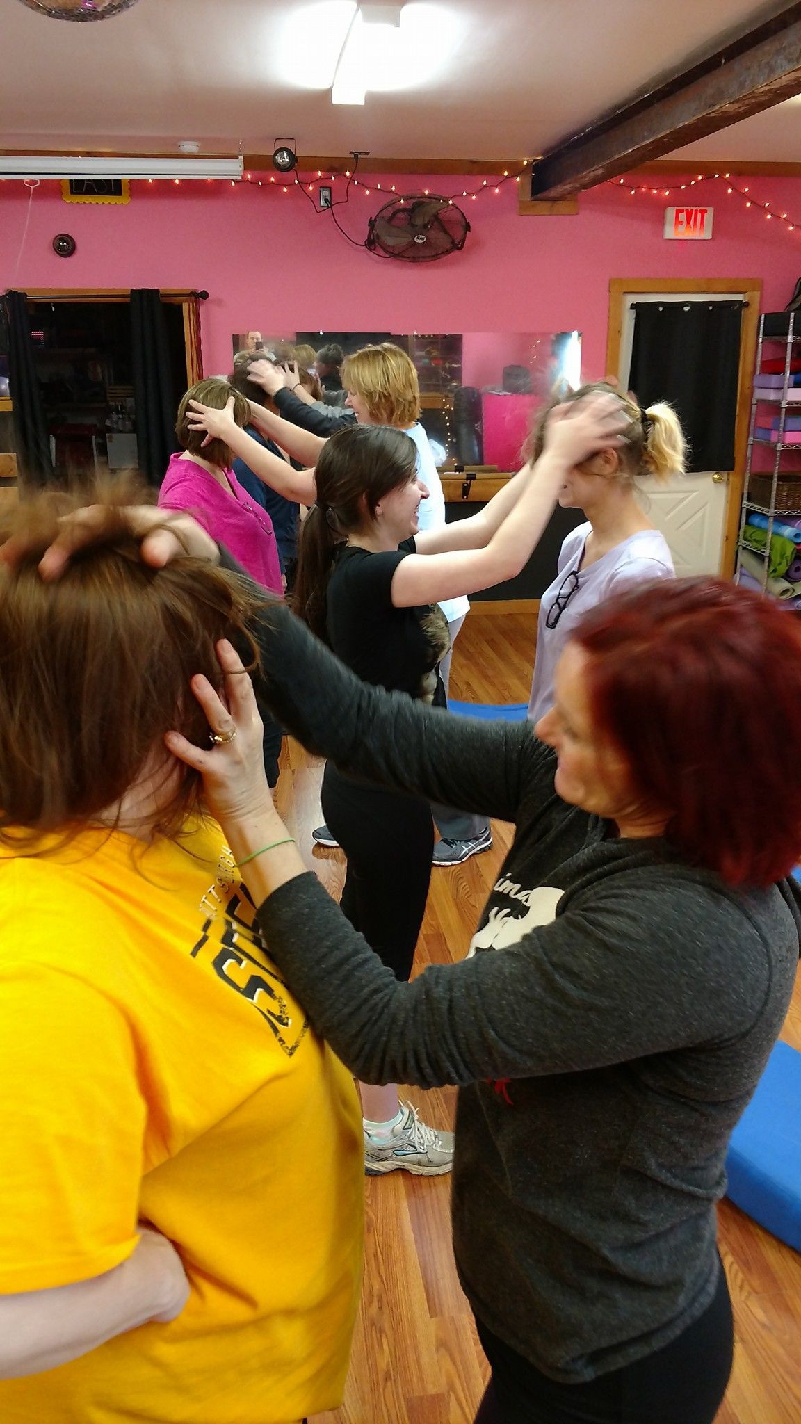 People in a room with pink walls are participating in a class, touching each other's heads