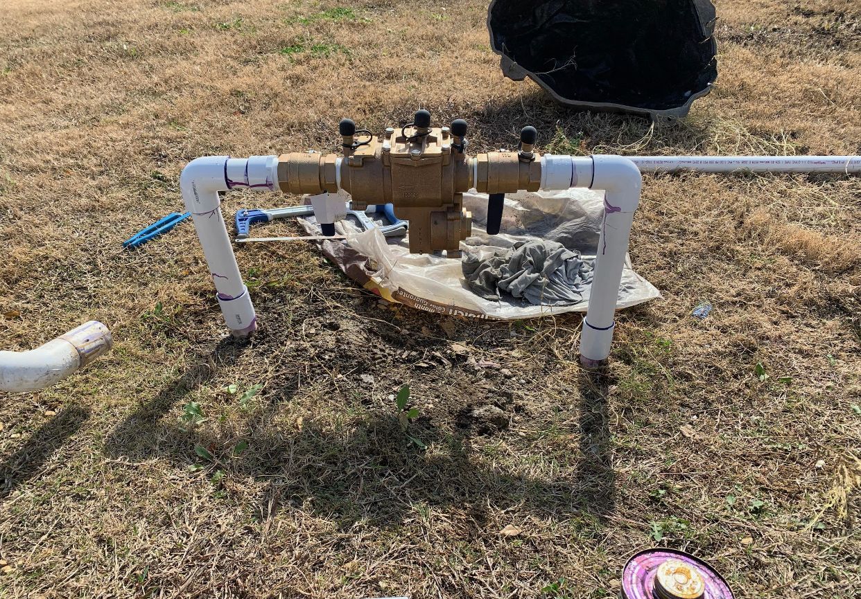 Irrigation valve assembly with PVC piping, set on dry grass.