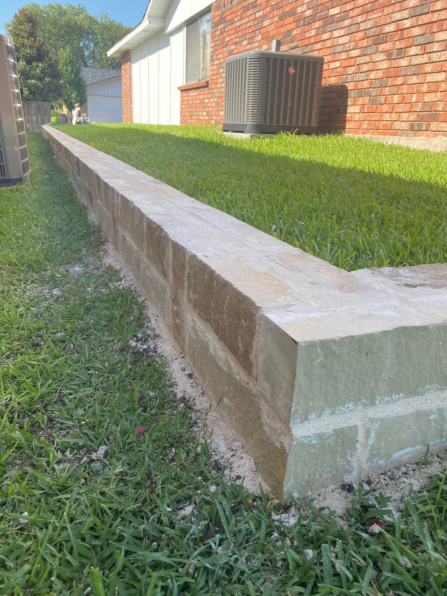 Low brick retaining wall along a grassy yard next to a brick building.