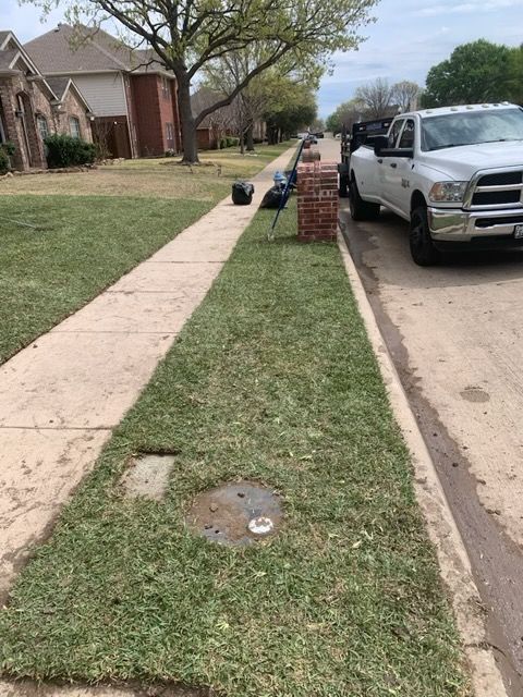 Lawn next to a sidewalk with a utility access point. A truck and bricks sit nearby, suggesting yard work.