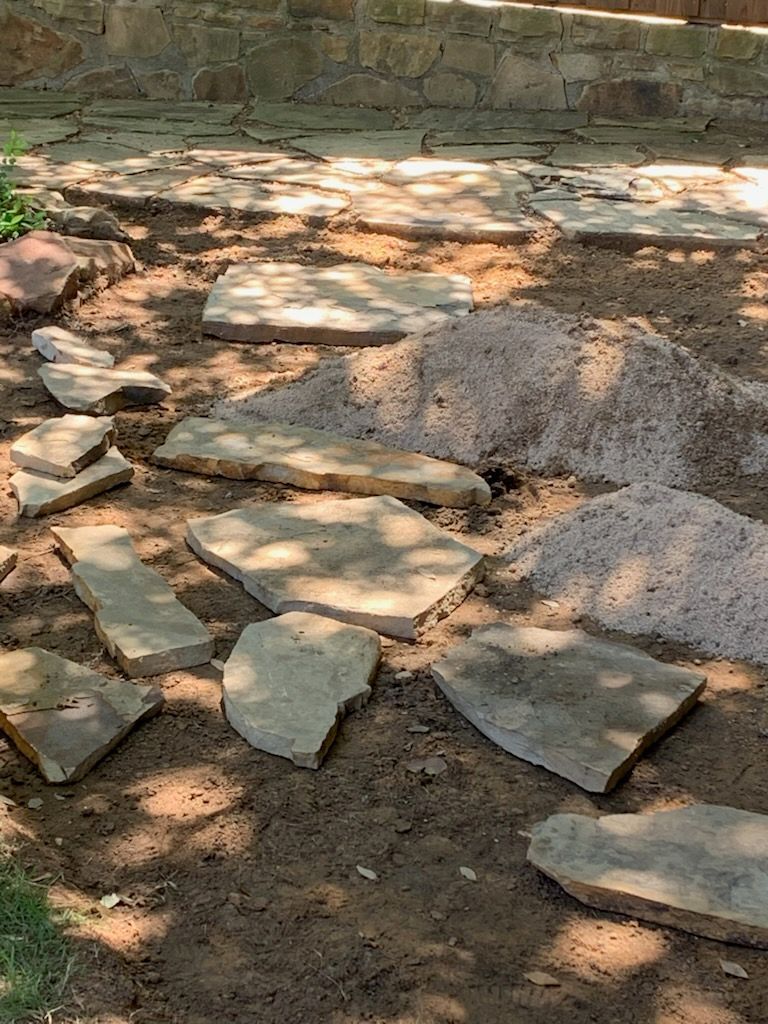 Stone pavers laid out in dirt, near a stone wall.
