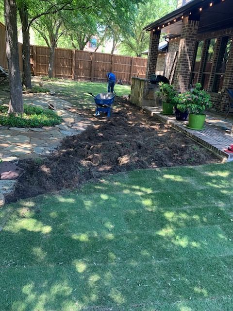 Person spreading mulch in a backyard with green grass and a house.