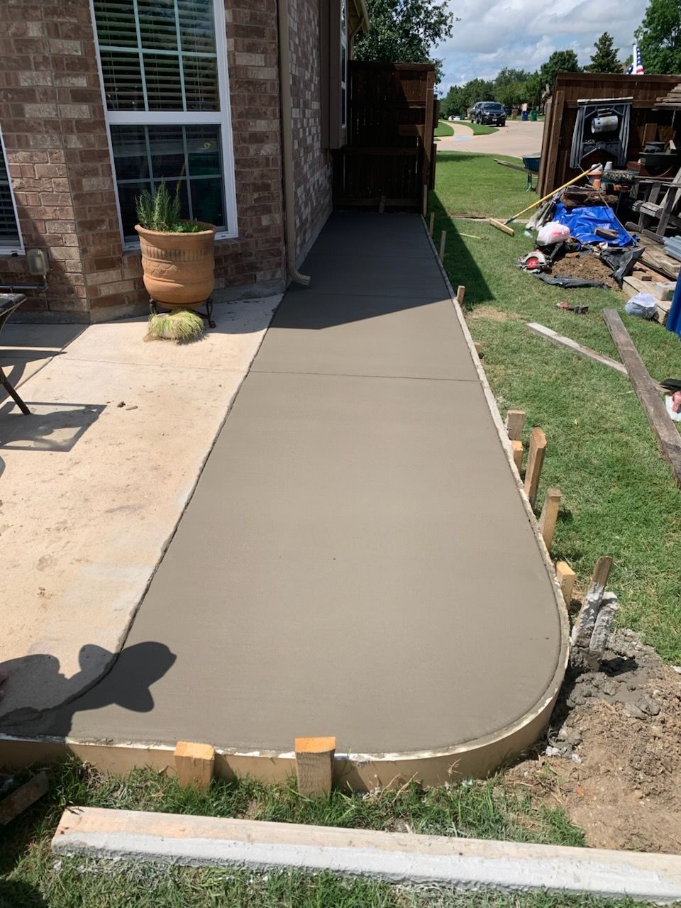 Newly poured concrete sidewalk with rounded edge, along a brick building and grass lawn.