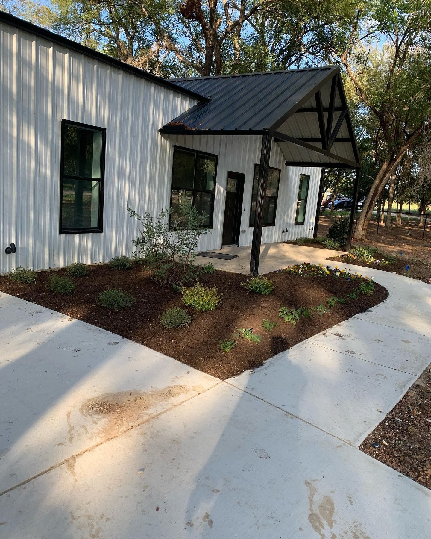Newly poured concrete walkway next to a brick house. Wood forms outline the curved edge, on a grassy lawn.