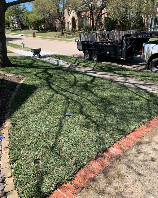 Sprinkler watering a green lawn in front of a brick house. Sunny day.