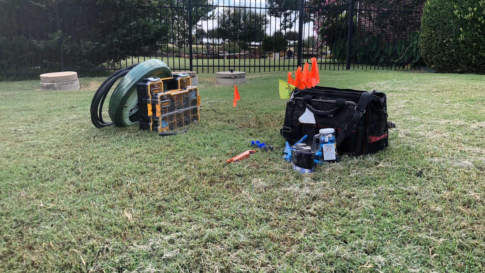 Lawn with equipment, including a toolbox and metal parts, near a fence in an outdoor setting.