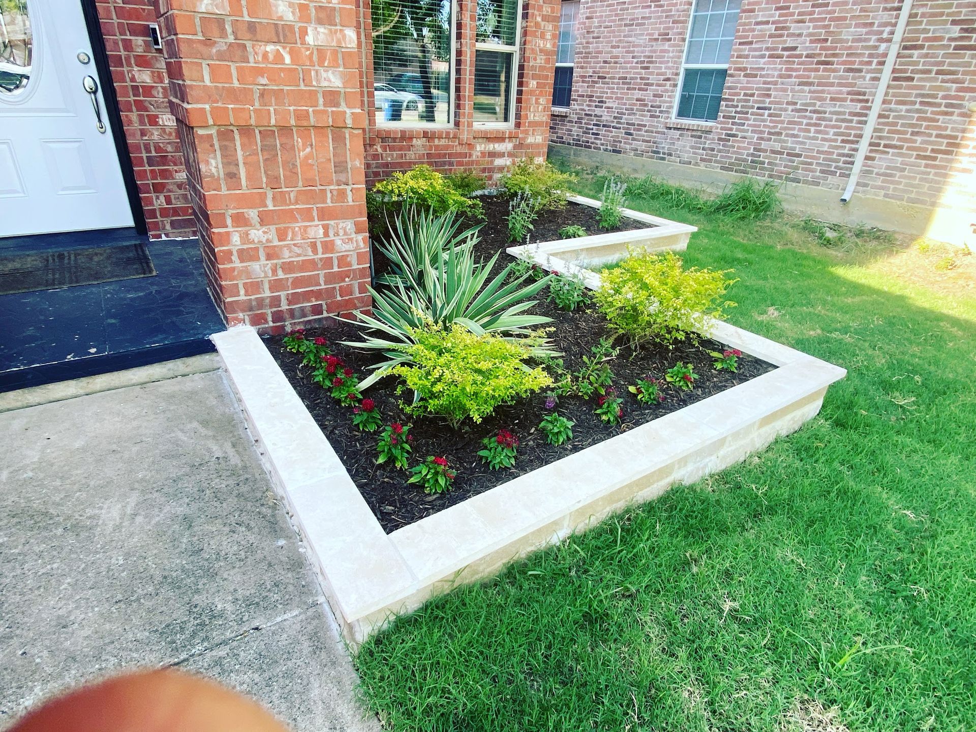 Raised garden beds with various plants in front of a brick building.