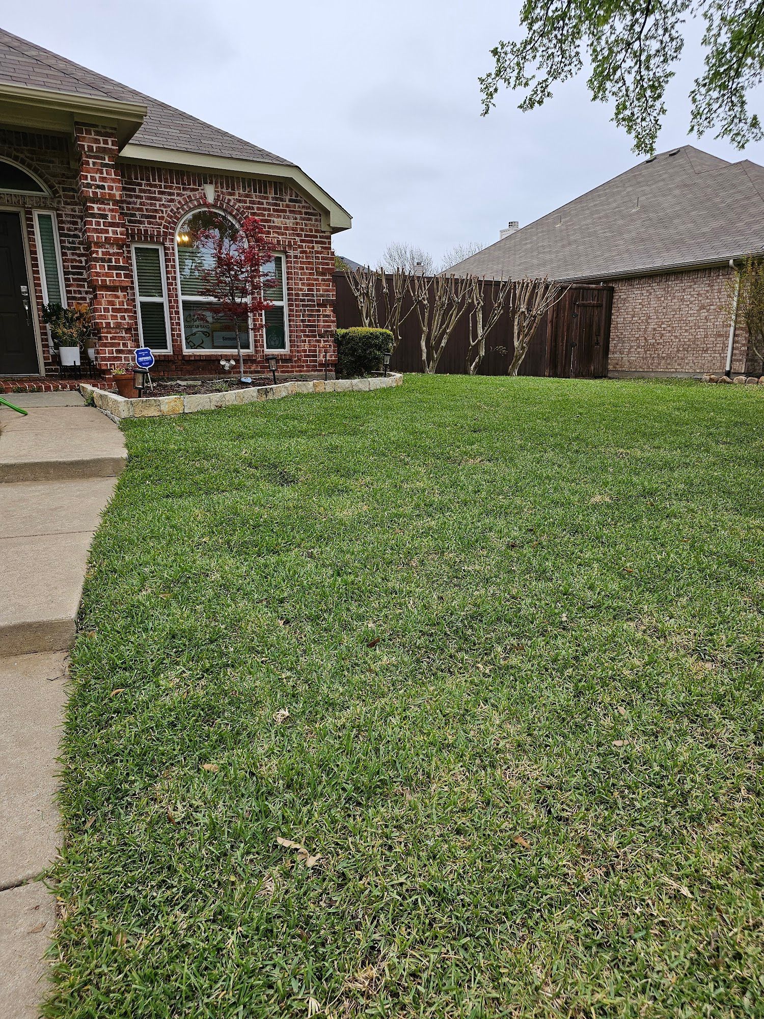 Landscaped yard with circular brick planter, trimmed bushes, and lush green grass.