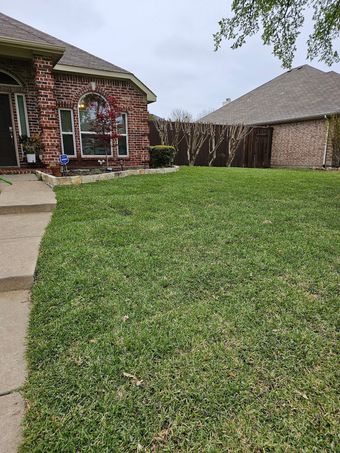 Landscaped yard with circular brick planter, trimmed bushes, and lush green grass.