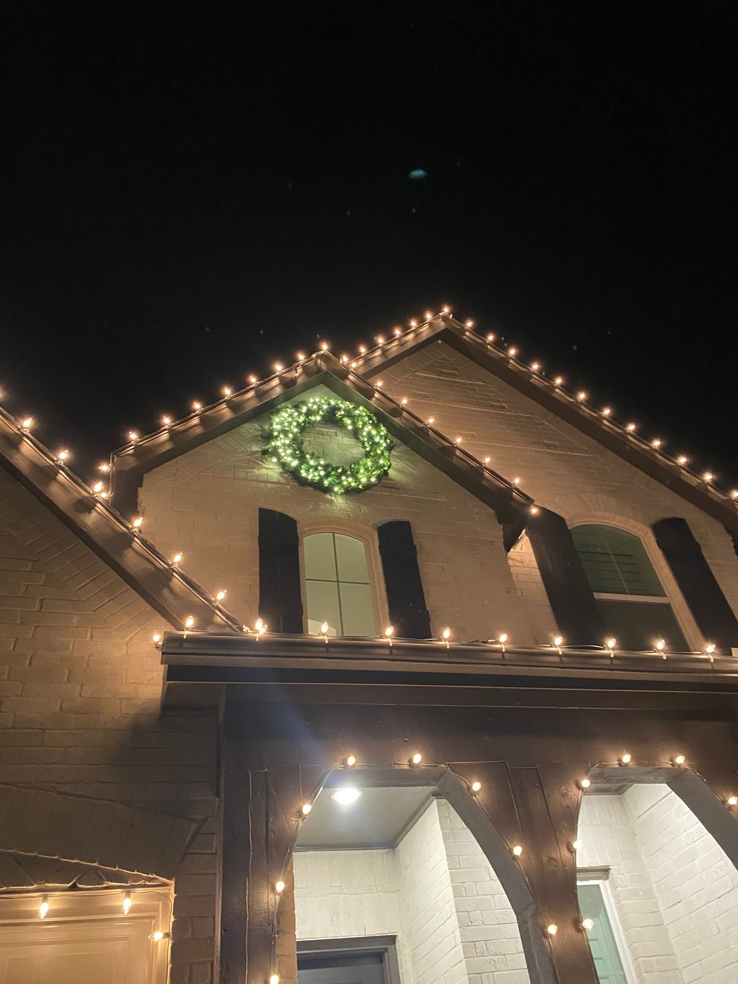 House exterior lit with Christmas lights; wreath on the roof.