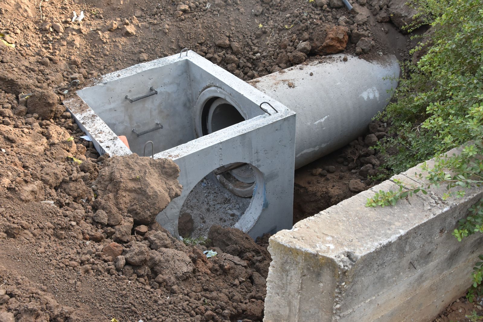 Concrete drainage system installation in a dirt trench, with pipe and square inlet.