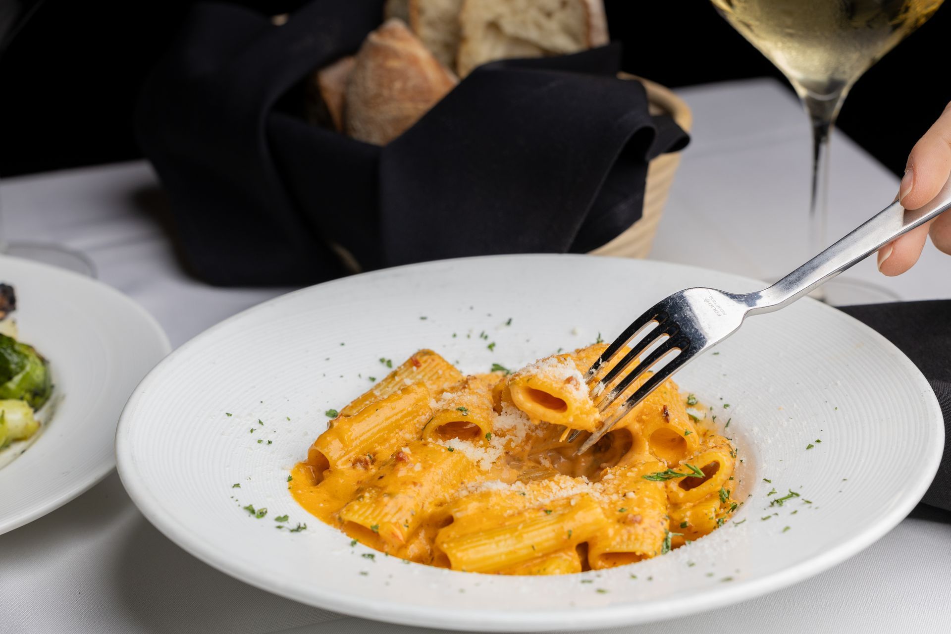A person is holding a fork over a plate of pasta.