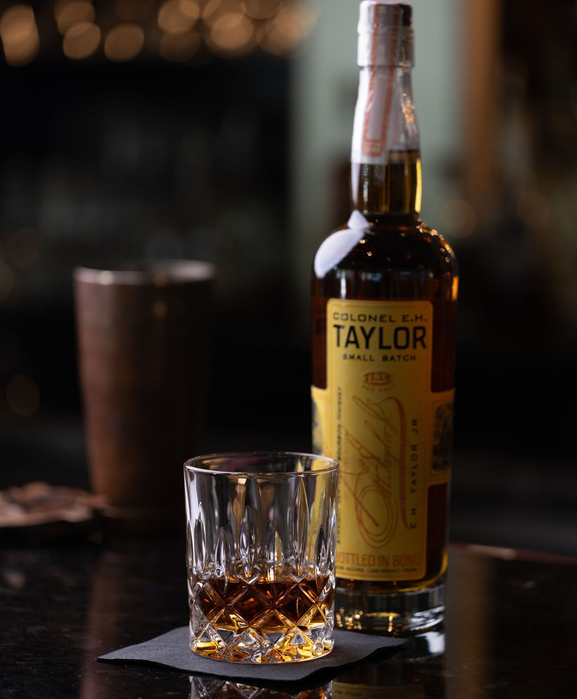 A bottle of taylor whiskey next to a glass of whiskey