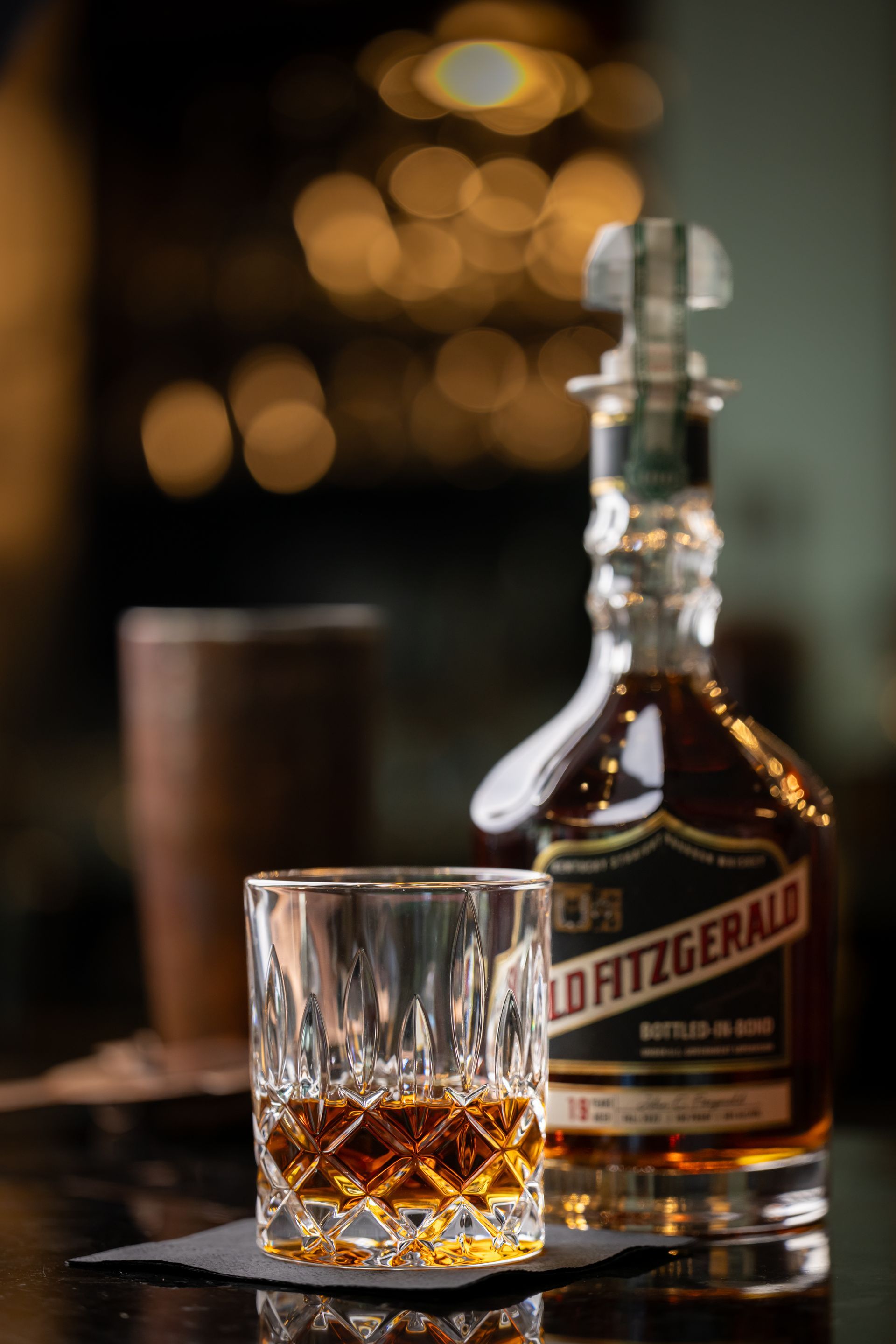 A bottle of old fitzgerald whiskey next to a glass of whiskey