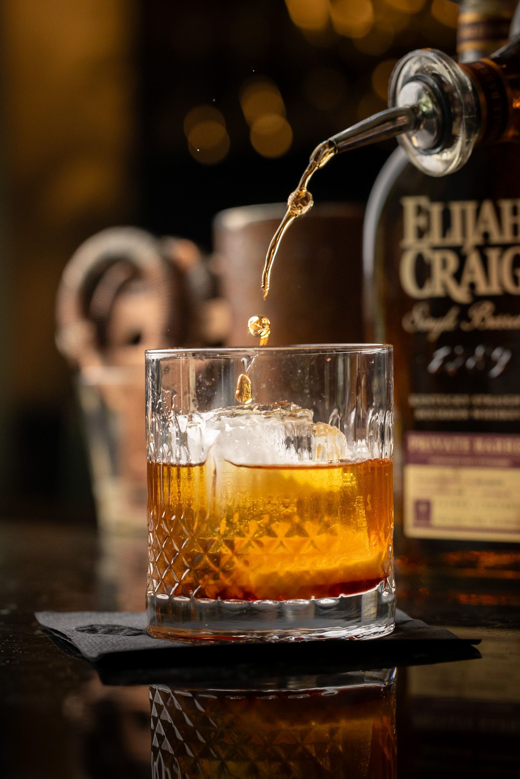 A glass of whiskey is being poured into a glass with ice.