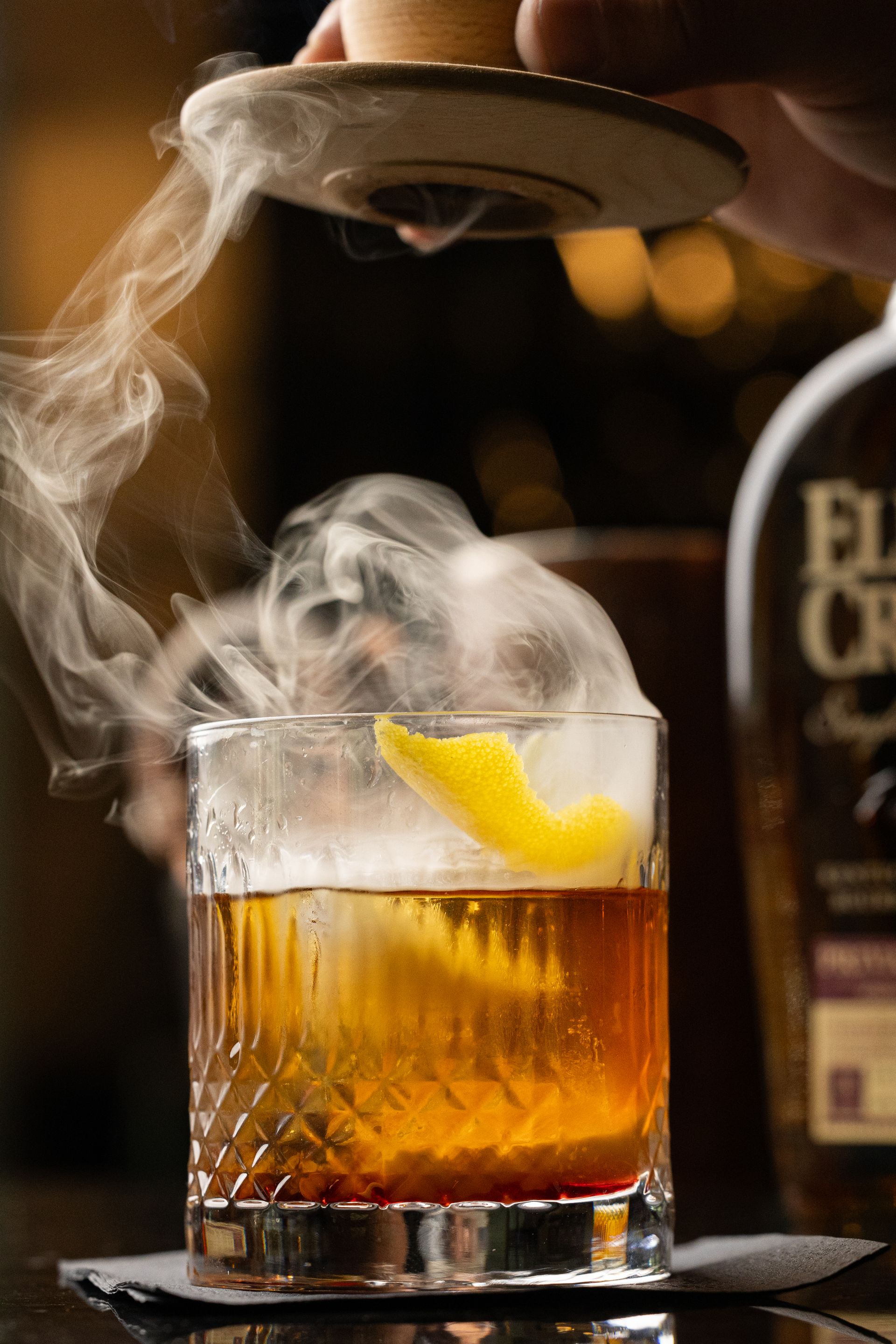 A person is pouring a drink into a glass with smoke coming out of it.