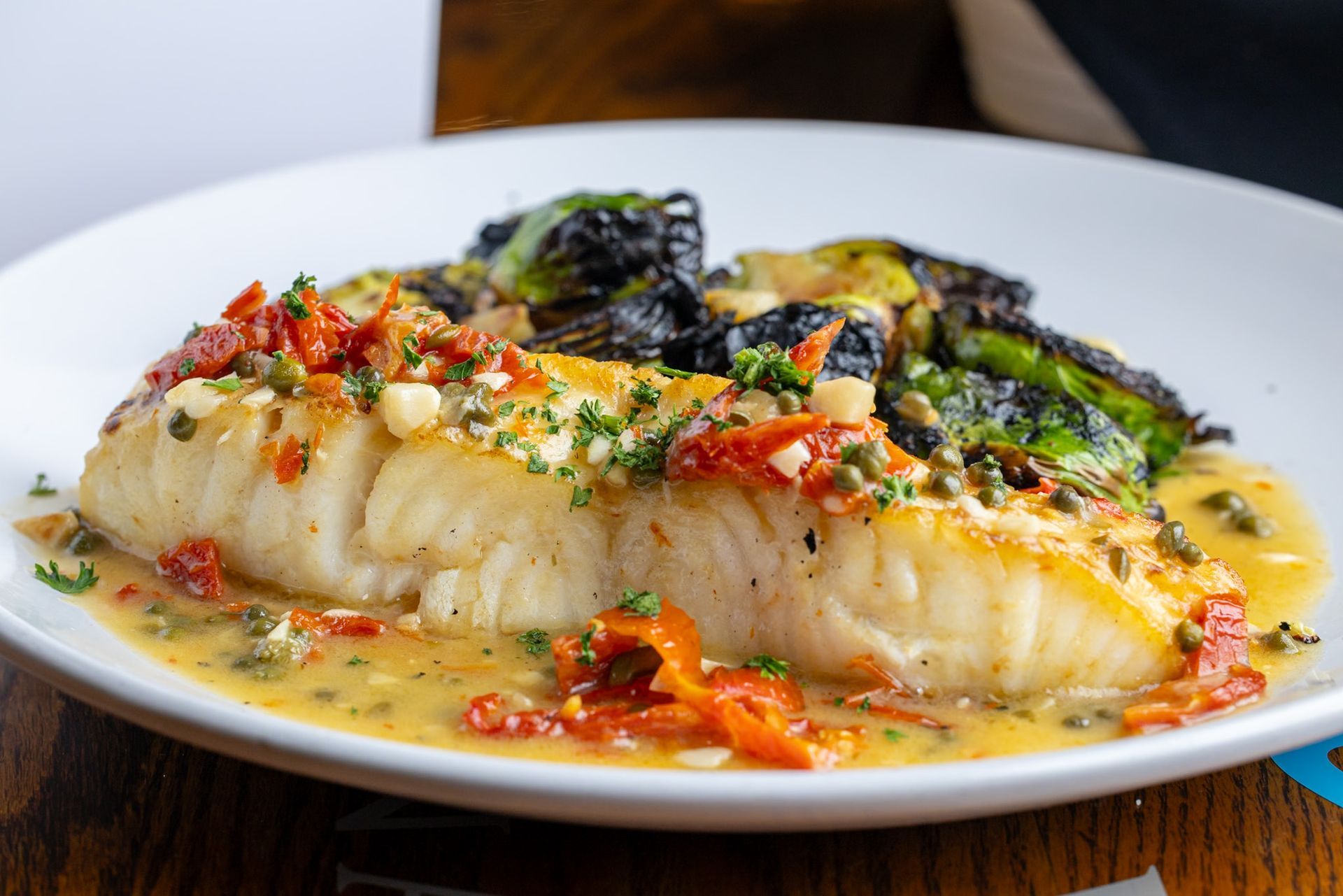 A white plate topped with a piece of fish and vegetables on a wooden table.