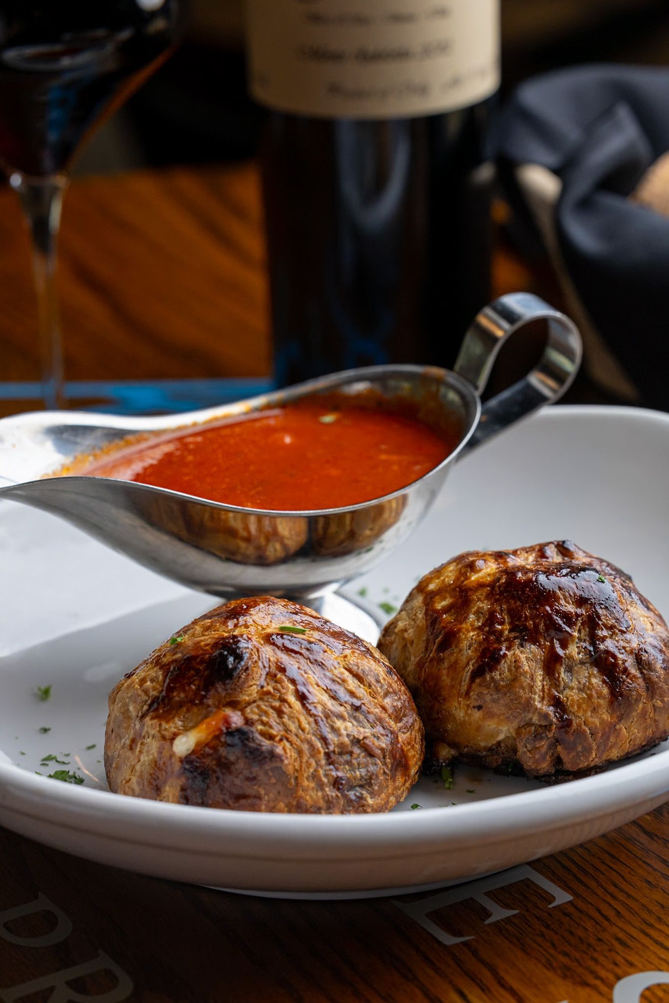 A white plate topped with meatballs and sauce next to a bottle of wine.