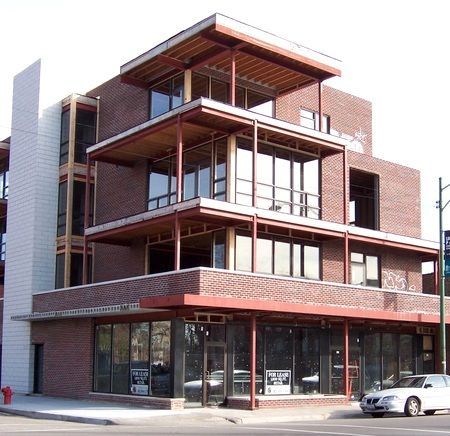 A white car is parked in front of a large brick building