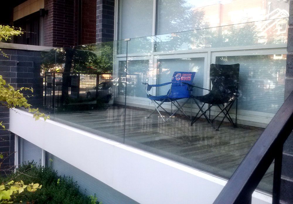 A balcony with a glass railing and two chairs on it.