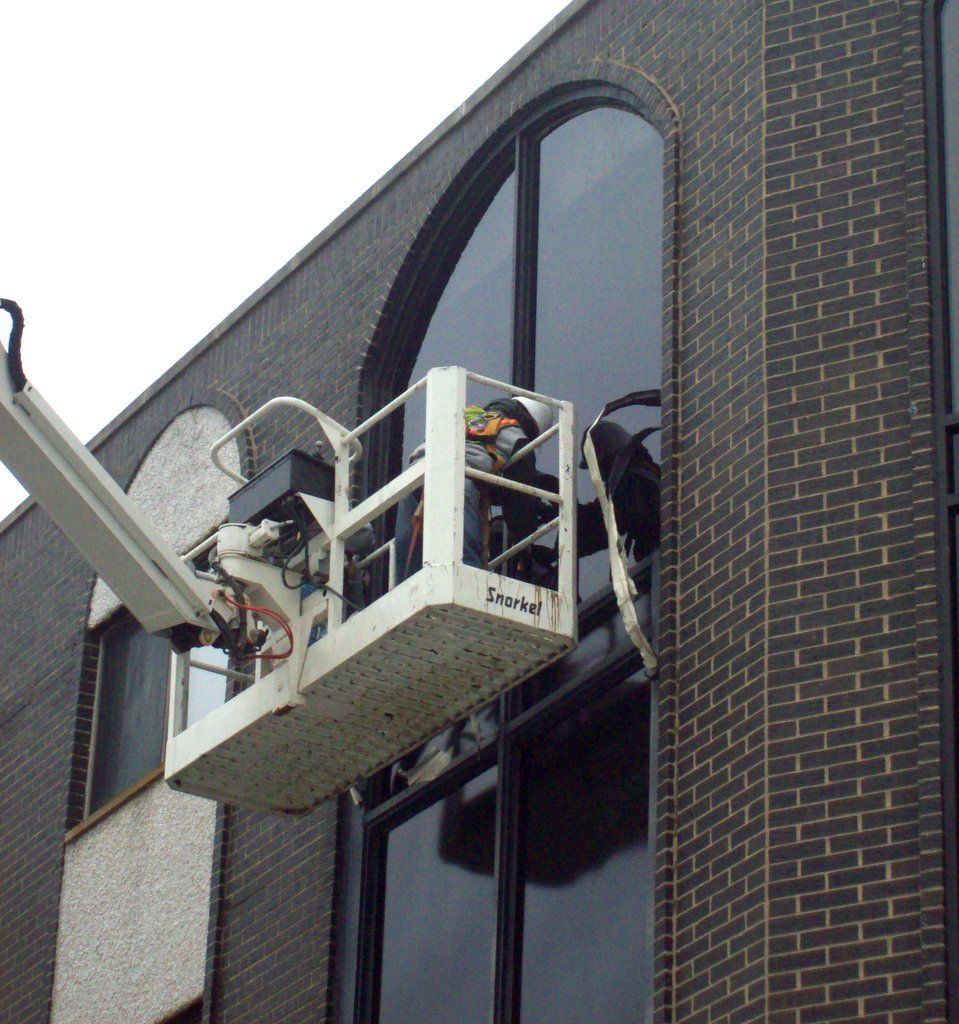 A man in a bucket is cleaning a window on a brick building