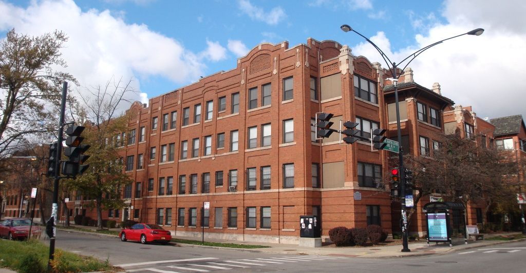 A red car is parked in front of a large brick building