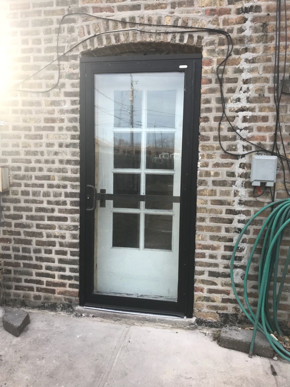 A black door is sitting on a brick wall next to a green hose.