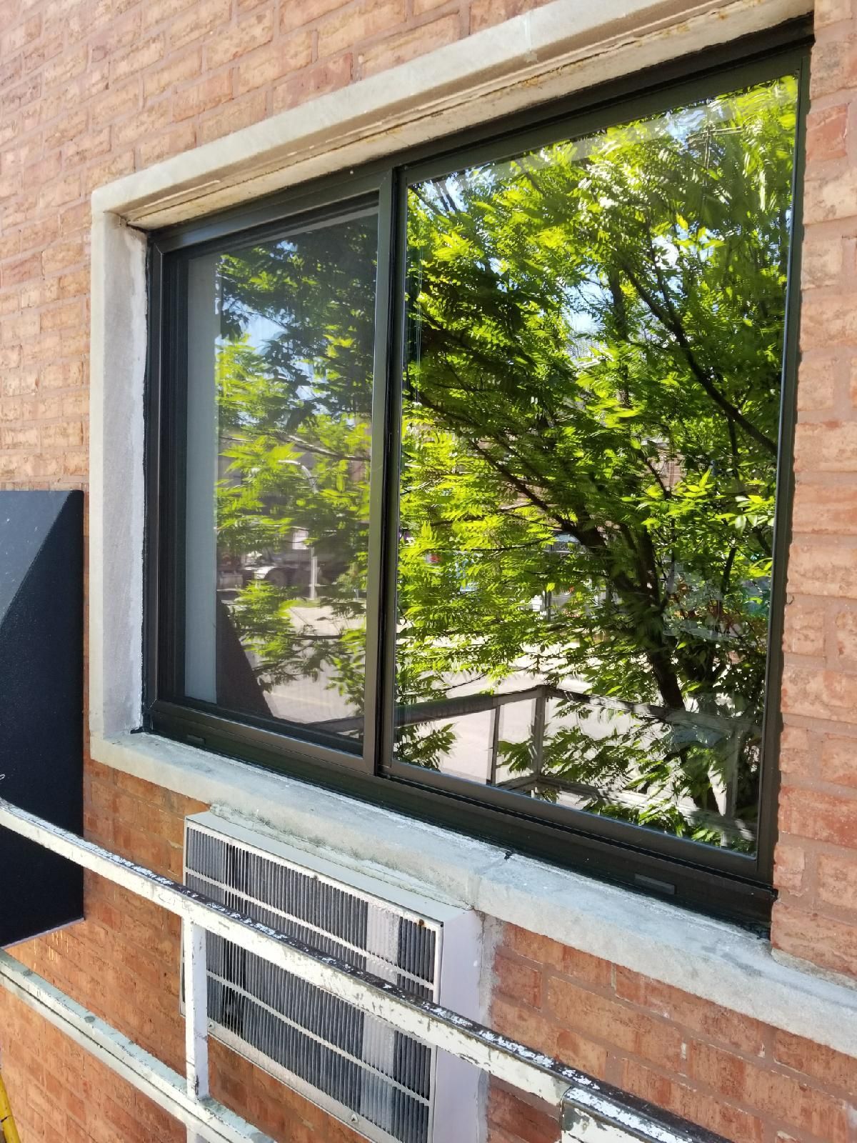 A large window on the side of a brick building with trees reflected in it.