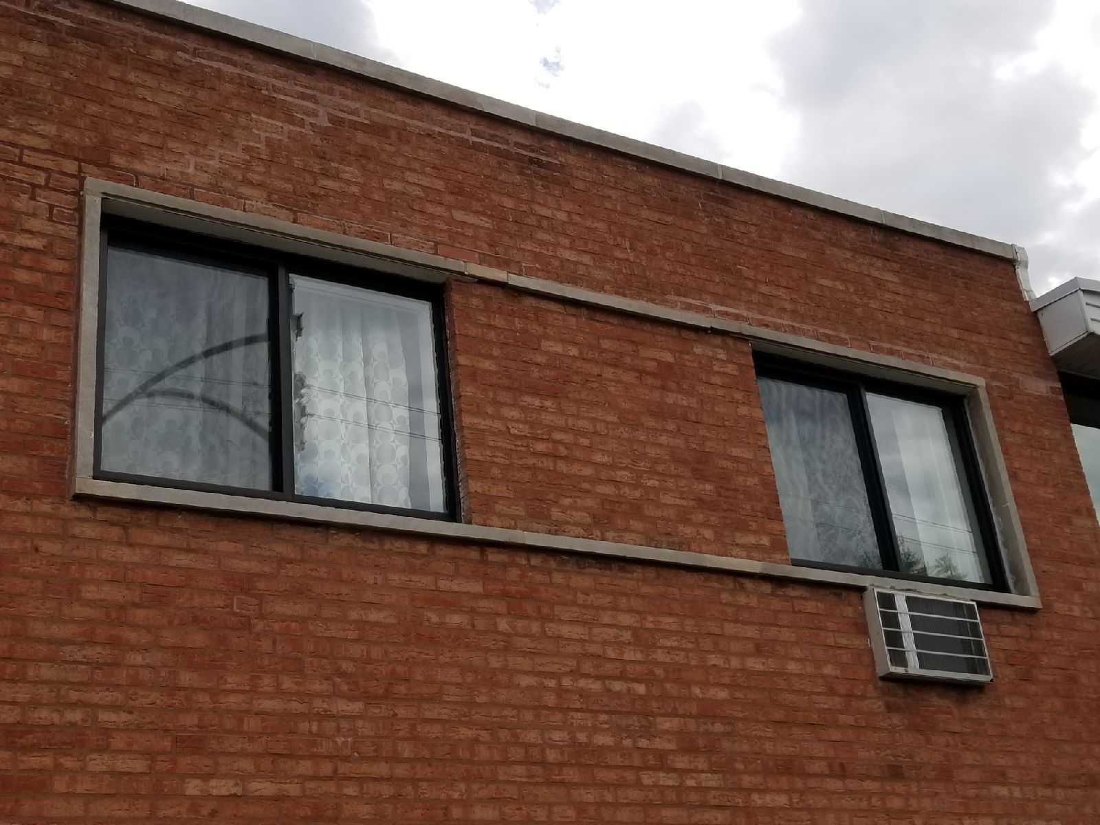 A brick building with two windows and an air conditioner on the side
