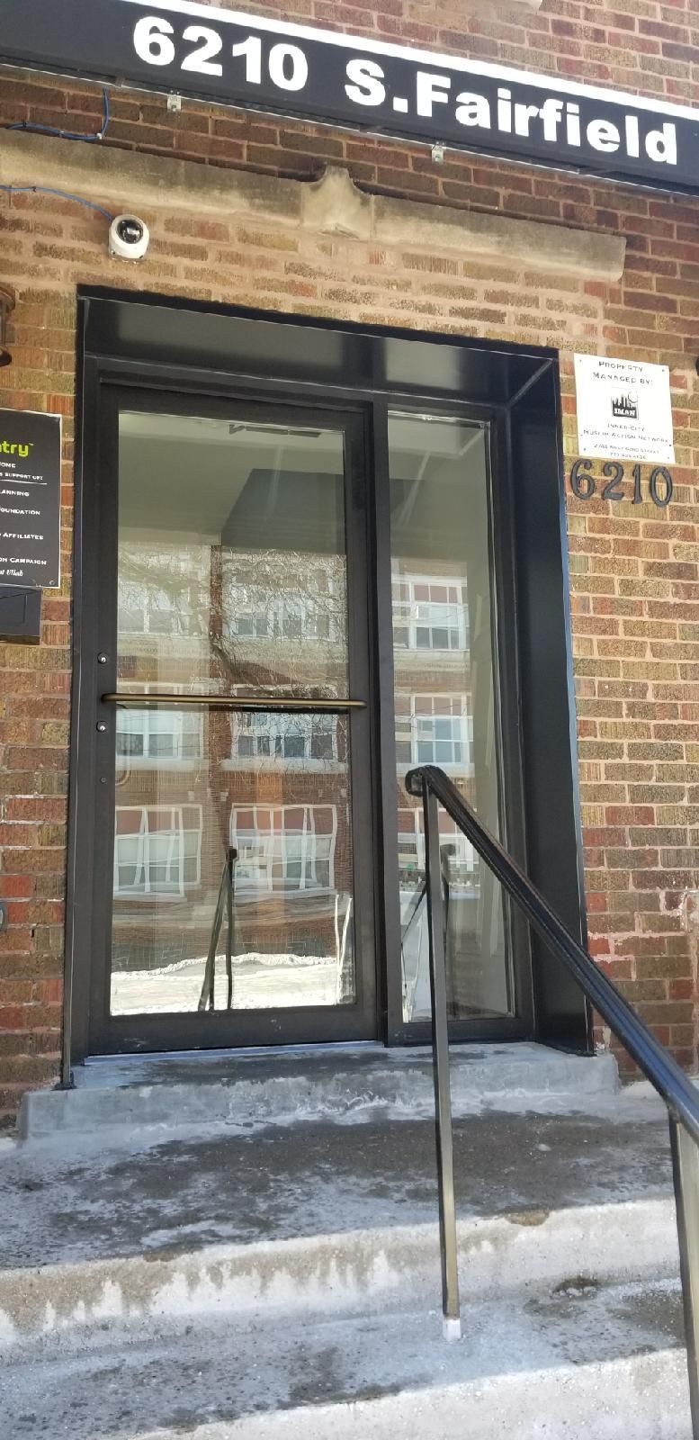 A brick building with a glass door and stairs leading up to it.