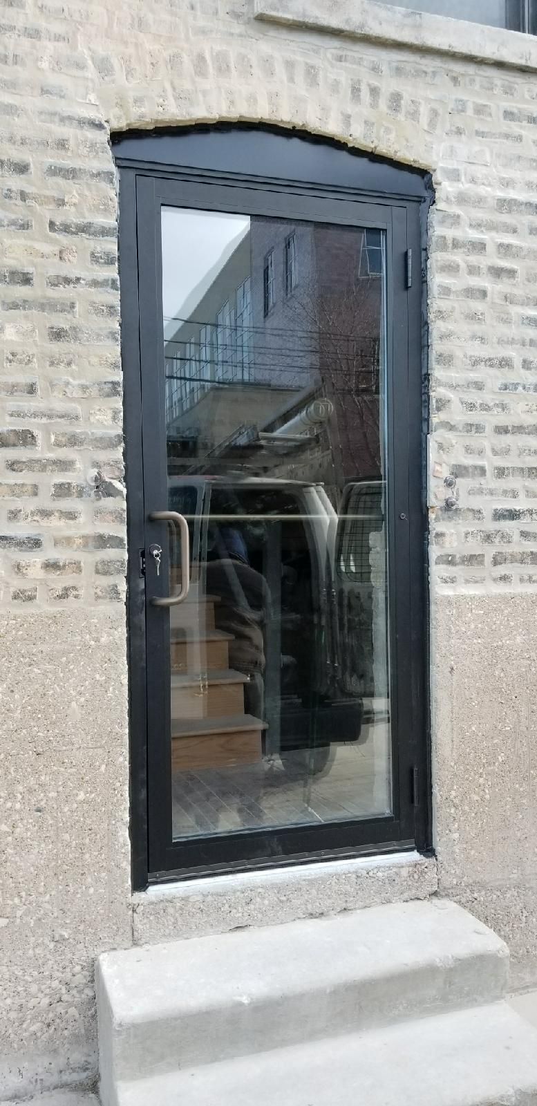 A black door with stairs leading up to it is on a brick building.
