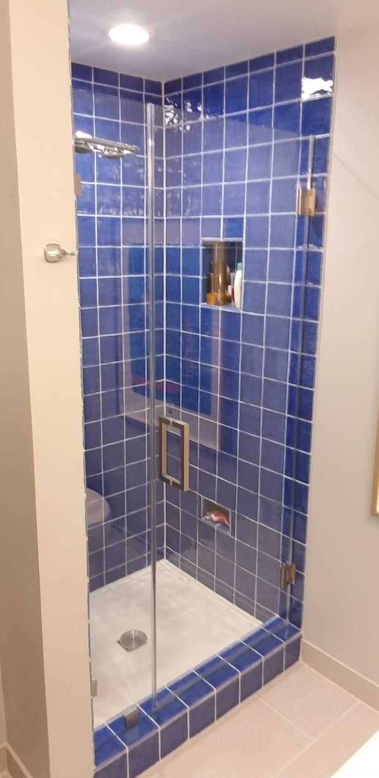 A bathroom with blue tiles and a walk in shower with a glass door.