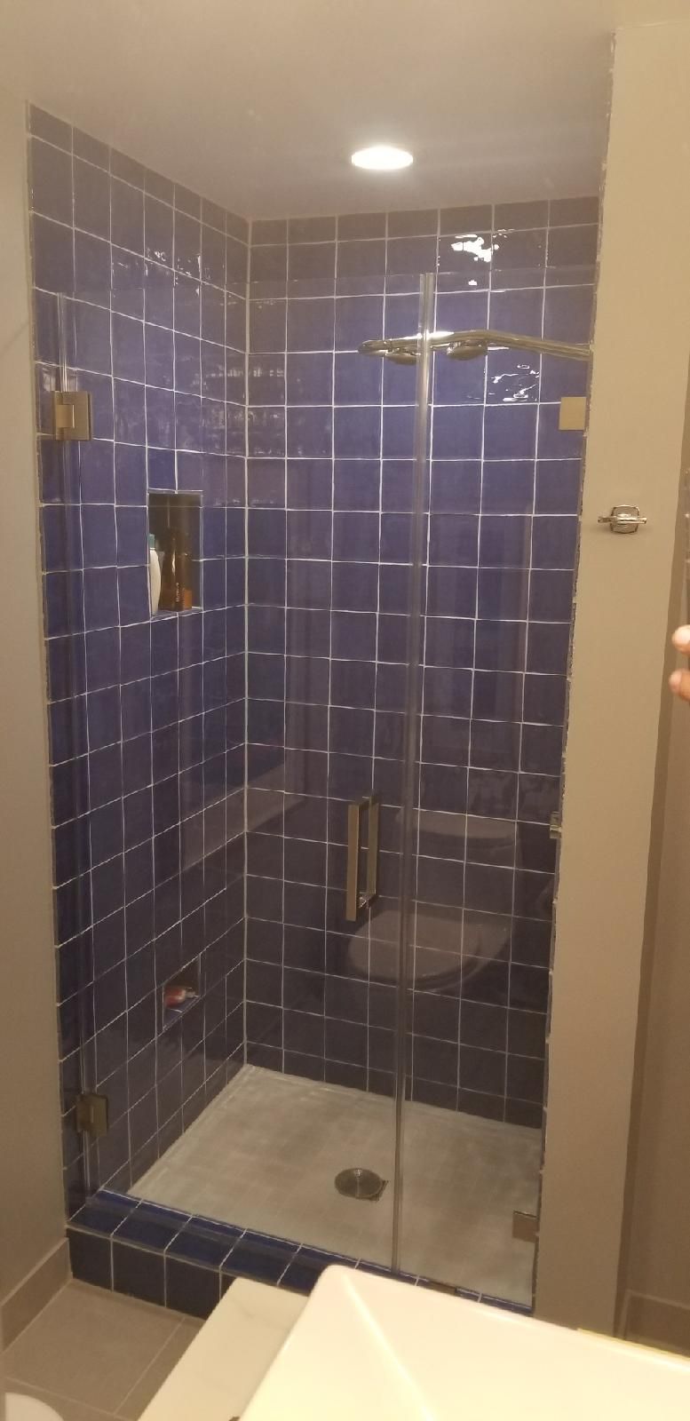 A bathroom with blue tiles and a walk in shower with a glass door.